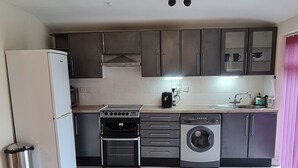 Een kleine keuken met een koelkast, fornuis, oven, wasmachine en een spoelbak.