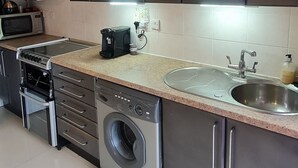 Een moderne keuken met roestvrijstalen apparatuur, een inbouwoven, magnetron en koffiezetapparaat, plus een wasmachine.