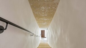 Un escalier étroit et bien éclairé, doté d’une rampe métallique, mène à une porte située en haut.