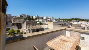 Une terrasse sur le toit, avec une table et des chaises en bois, offrant une vue sur un paysage urbain composé d’un mélange de bâtiments modernes et traditionnels.