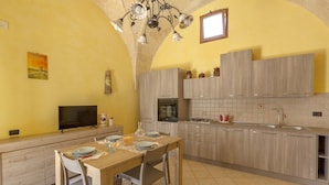 Une cuisine avec une table à manger pour quatre personnes, un téléviseur et un mur recouvert de carreaux.