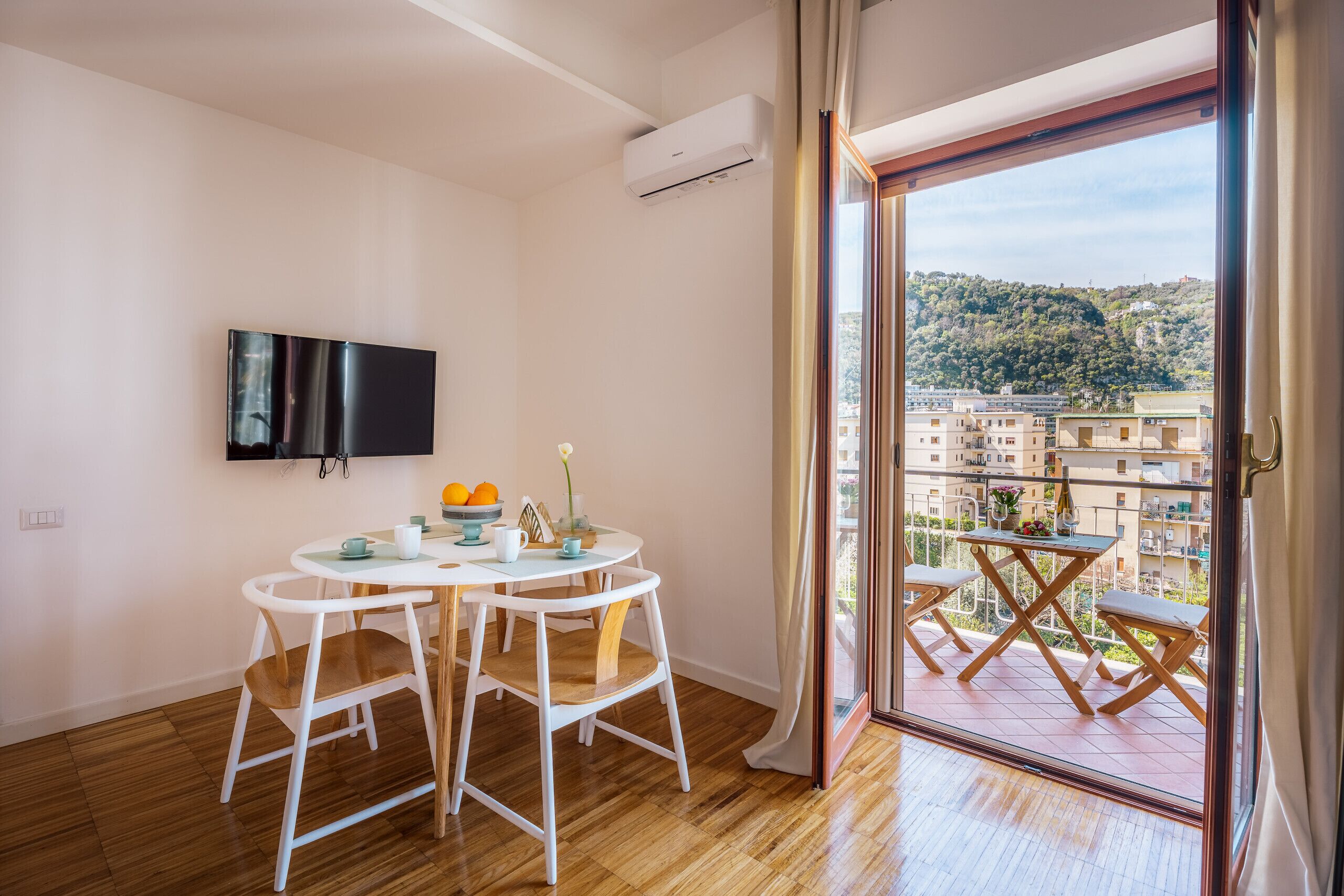 Un appartamento moderno con un balcone, una zona pranzo con tavolo e sedie e una TV a parete.