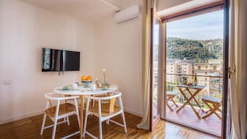 Un appartamento moderno con un balcone, una zona pranzo con tavolo e sedie e una TV a parete.