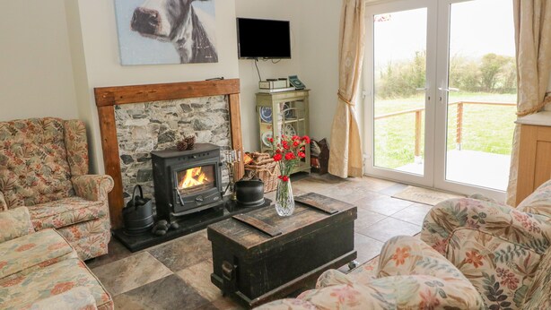 A cozy living room with a stone fireplace, floral-patterned sofas, a television, and a view of the outdoors through a sliding glass door. - SHANDRUM BROOK, pet friendly, country holiday cottage in Charleville (Charleville)