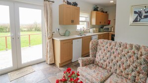A spacious living area with a sofa and a dining table, a kitchen with wooden cabinets, and a sliding glass door leading to a balcony. - SHANDRUM BROOK, pet friendly, country holiday cottage in Charleville (Charleville)