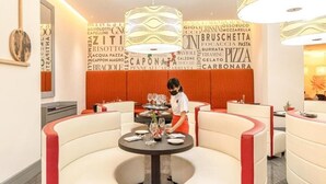 Restaurant amb interior modern, amb seients de color blanc i vermell corbat, personal d'atenció i una paret amb paraules relacionades amb l'alimentació.