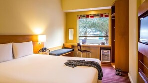 Habitació d'hotel amb un llit, escriptori, cadira, taula petita, televisió i finestra amb vista a palmeres.