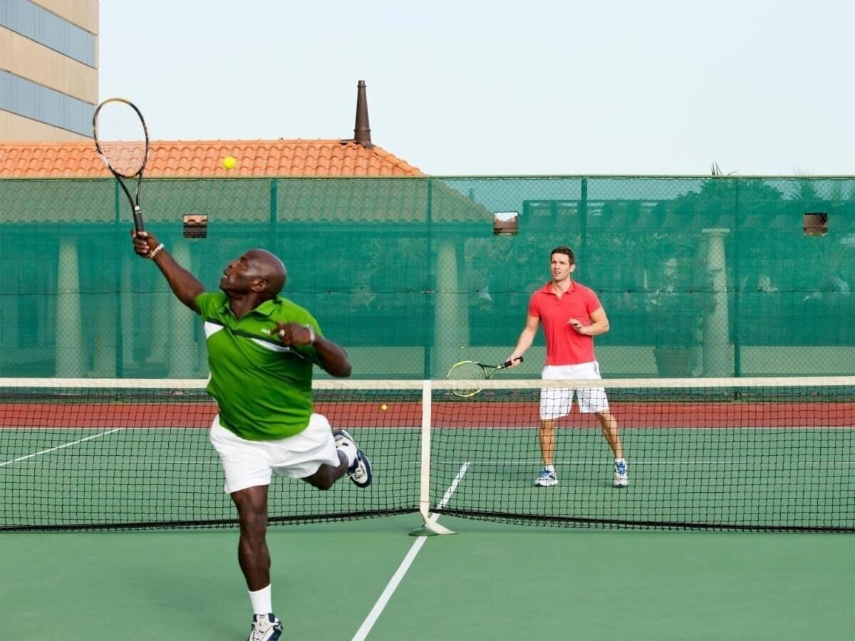 A tennis court with two players in action, one in green and the other in red.