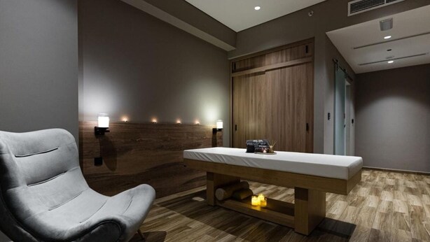 Une salle de massage moderne équipée d’une table de massage, d’un fauteuil de massage et d’un système d’éclairage mural.