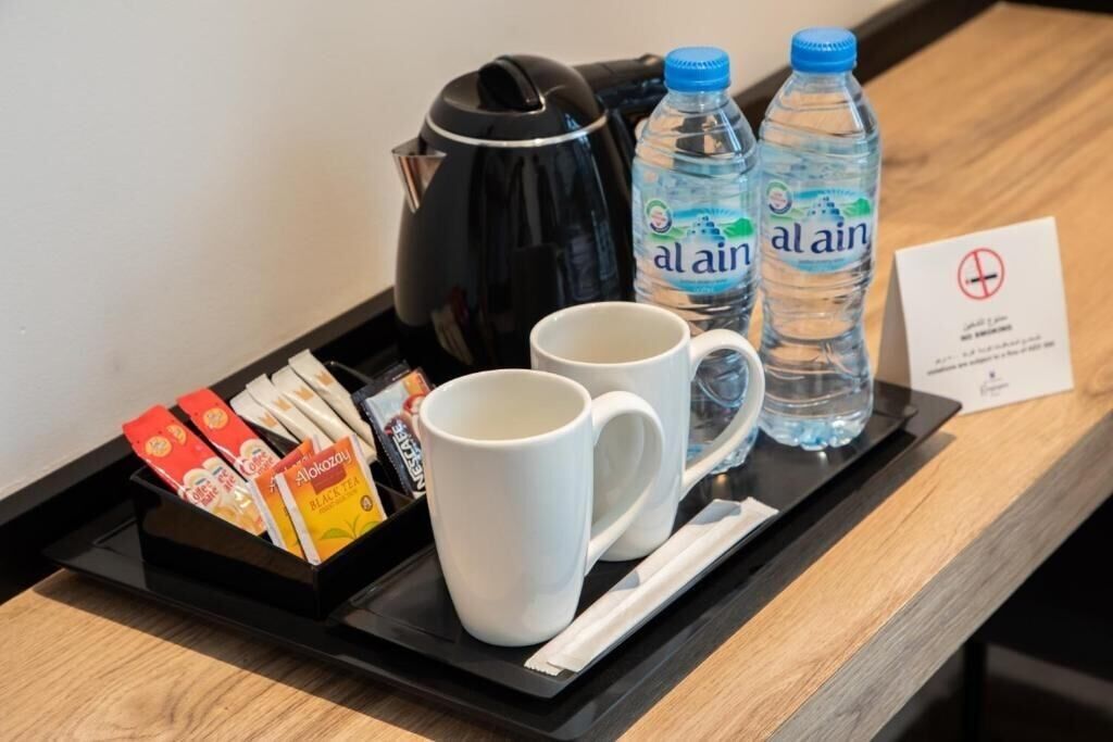 A tray with a black coffee maker, two white mugs, two bottles of water, and a box of tea bags.