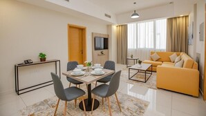 Een moderne woonkamer met een bank, een eettafel met stoelen, een aan de muur bevestigde televisie en een groot raam met gordijnen.