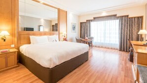A hotel room with a large bed, a desk, a chair, a small table, a mirror, and a window with curtains. - Standard Room Near Capital Park By E R (أبو ظبي)