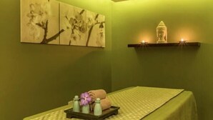 A spa room with a green wall, a massage table, a Buddha statue, and a painting of flowers. - Standard Room Near Capital Park By E R (أبو ظبي)