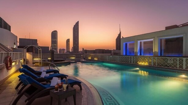 A rooftop pool with lounge chairs and a city skyline at sunset. - Standard Room Near Capital Park By E R (أبو ظبي)