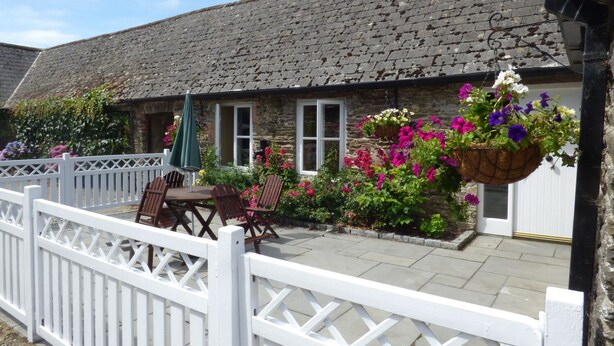 A stone cottage with a thatched roof, a white picket fence, and a patio with outdoor furniture. - ROSEMOUNT COACH HOUSE, pet friendly in Enniscorthy, County Wexford (Marshalstown)