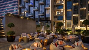 Un lounge en la azotea con asientos al aire libre, plantas en macetas y vistas a un edificio moderno.