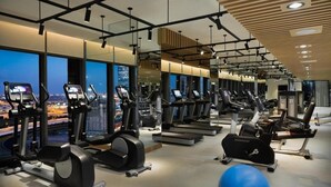 Un gimnasio moderno con cintas de correr, elípticas y equipo de pesas, que cuenta con amplias ventanas con vista a la ciudad.