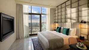 Habitación de hotel con una cama grande, un televisor montado en la pared, un balcón con vistas y un paisaje urbano visible a través de la ventana.