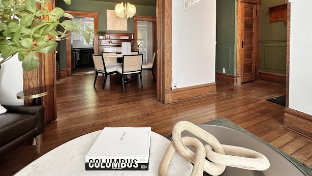 Un comedor con una mesa y sillas de madera, una araña y un letrero que dice 'Columbus'.