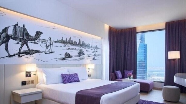 Habitación de hotel moderna con una cama grande, una mesita de noche, un espacio para sentarse y vistas a la ciudad.