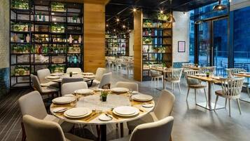 A restaurant with round tables set for dining, surrounded by shelves of plants and books.