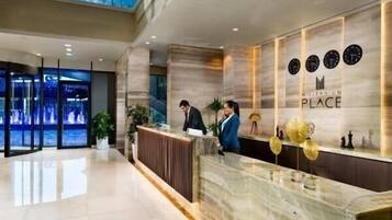 A modern hotel reception area with a marble counter, a glass wall, and a high ceiling with natural light.