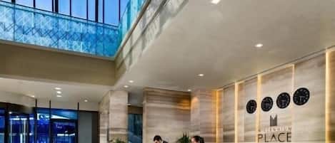 A modern hotel reception area with a marble counter, a glass wall, and a high ceiling with natural light.