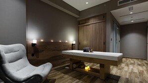 A massage room with a wooden bench, a massage table, and wall-mounted lights.