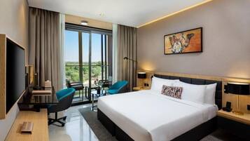 A modern hotel room with a large bed, a desk with a chair, a small table, and a balcony with a view.