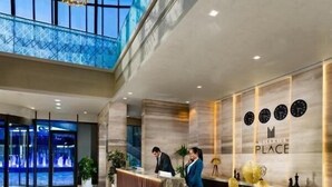 A modern hotel reception area with a marble counter, a glass wall, and a ceiling with a geometric light fixture. - Deluxe Room in Mirdif By E R (Dubai)