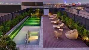 Zona de piscina en la azotea con vistas al horizonte de la ciudad, incluyendo un edificio distintivo con estructura en forma de vela.