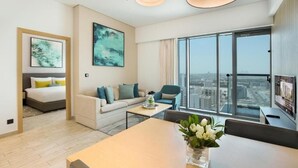 Een moderne hotelkamer met een bed, een sofa, een eettafel en een groot raam met uitzicht op de stad.
