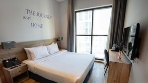 A hotel room with a large bed, a bedside table with a phone and tissues, a TV on the wall, and a window with curtains. - Standard Room Near Jadaf Metro (Dubai)