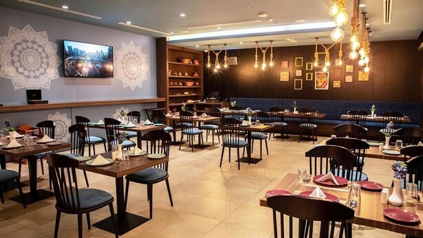 A restaurant with multiple dining tables and chairs, a television mounted on the wall, and decorative wall art. - Standard Room Near Jadaf Metro (Dubai)