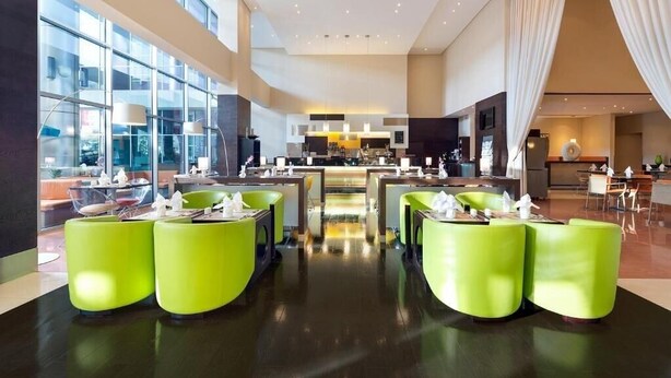 Un hall d’hôtel moderne avec un bar central, des sièges d’un vert vif et de grandes fenêtres offrant une vue sur la ville.