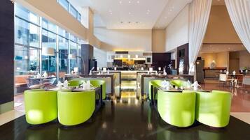 Un hall d’hôtel moderne avec un bar central, des sièges d’un vert vif et de grandes fenêtres offrant une vue sur la ville.