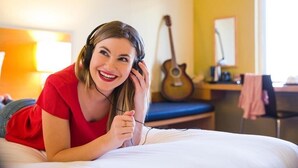 Une personne allongée sur un lit dans une pièce, avec une guitare et un bureau en arrière-plan.