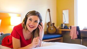 Une personne allongée sur un lit dans une pièce, avec une guitare et un bureau en arrière-plan.