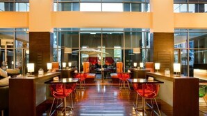 Un hall d’hôtel moderne doté d’un bar central, de sièges avec des fauteuils rouges et de grandes fenêtres offrant une vue sur la ville.