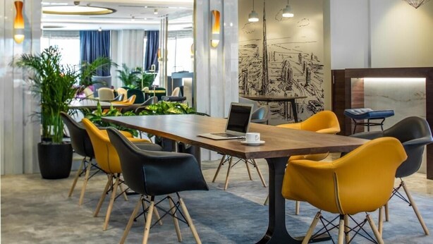A modern conference room with a long table, yellow and black chairs, and a laptop on the table.