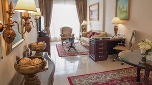A well-furnished hotel room with a sofa, armchair, desk, and decorative items.