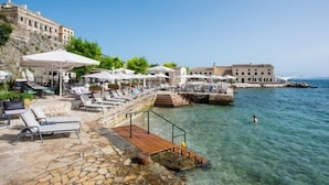 Un hotel frente al mar con terraza exterior, aguas cristalinas y un sendero de piedra que conduce al mar.