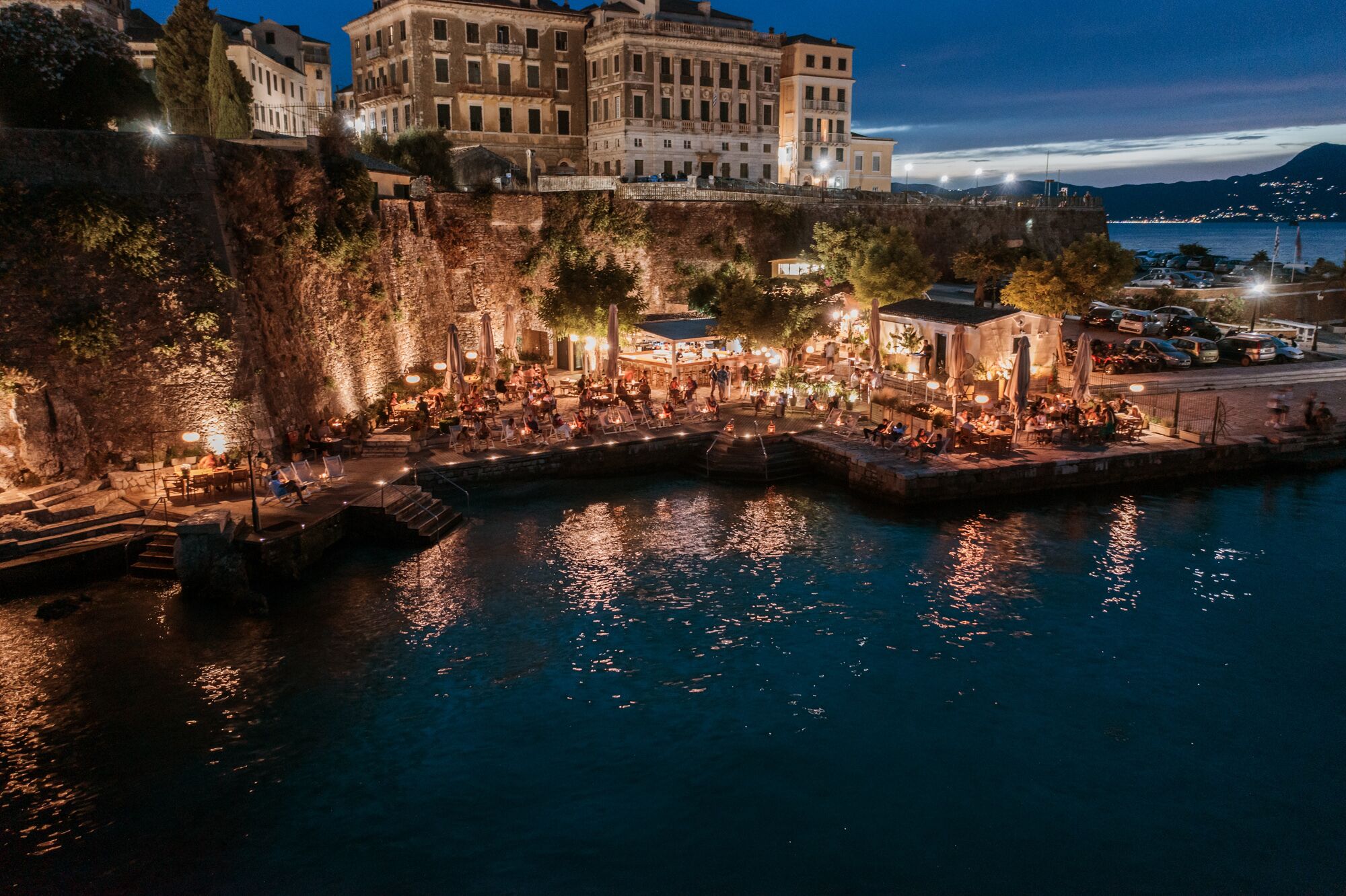 Restaurante frente al agua con terraza, paredes de piedra y vistas a edificios históricos.