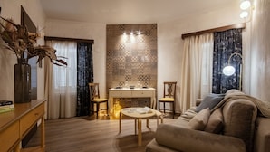Un salón con un sofá, una mesita y una chimenea. Hay cortinas en las ventanas y un jarrón con plantas secas sobre una mesita auxiliar.