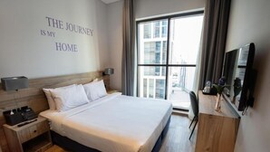 Une chambre d’hôtel avec un grand lit, une table de chevet avec un téléphone et des mouchoirs, un téléviseur posé sur une commode en bois, et une fenêtre donnant sur la ville.