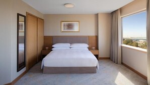 Hotellihuone, jossa on suuri sänky, yöpöytä, seinällä oleva taulu ja ikkunasta avautuva näkymä kaupunkiin.