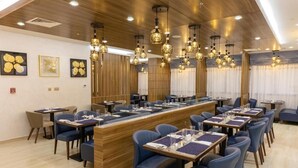 A modern dining area with a long wooden counter, blue upholstered chairs, and hanging pendant lights. - Studio Apartment Near Century Mall By E R (الفجيرة)