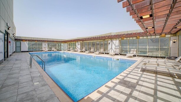 An indoor swimming pool with clear blue water, surrounded by lounge chairs and a glass wall. - Studio Apartment Near Century Mall By E R (الفجيرة)