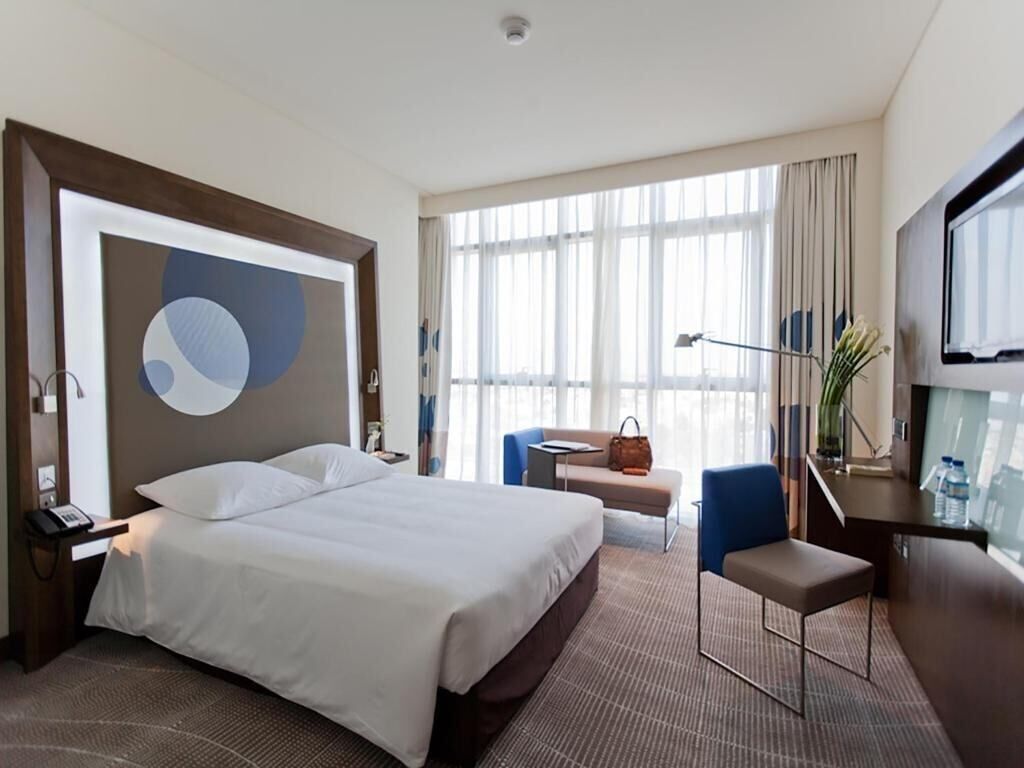A hotel room with a large bed, a desk, a chair, a sofa, and a TV.