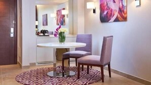 Una moderna camera d'hotel con un tavolo rotondo, due sedie, un tappeto decorativo e un grande quadro astratto appeso alla parete.